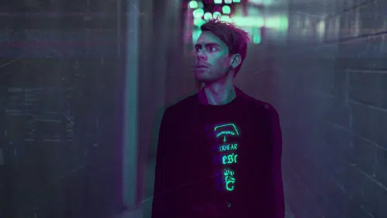 A man standing in a hallway with neon lights.