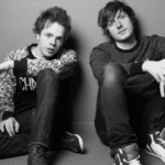 A black and white photo of two young men sitting on the floor.