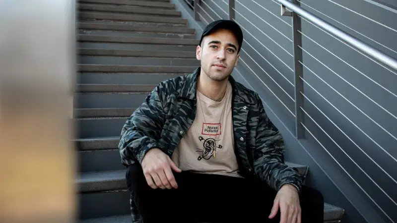 A man sitting on stairs wearing a camouflage jacket.