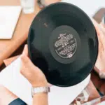 A man holding a vinyl record on a table.