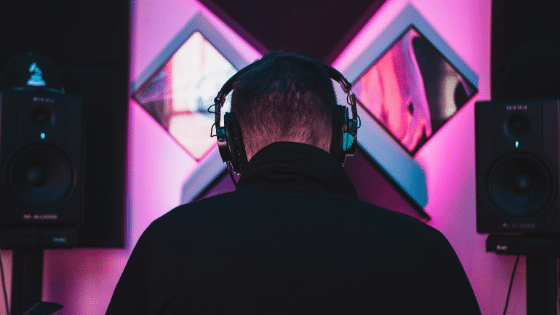 A man wearing headphones in front of a pink wall.