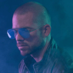 A man wearing sunglasses in front of a blue background.