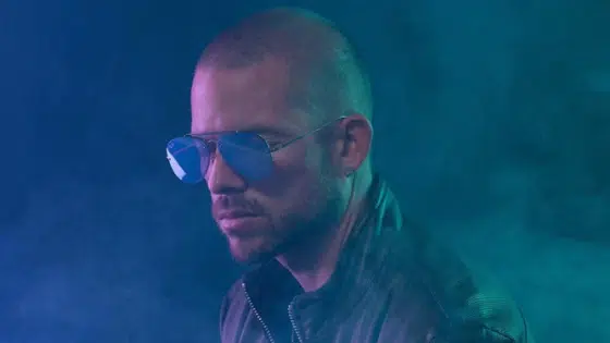 A man wearing sunglasses in front of a blue background.