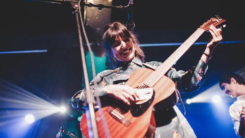 A woman playing an acoustic guitar on stage.