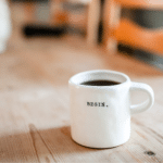 A white coffee mug sits on a wooden table.