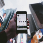 A person holding up a cell phone in front of a billboard.