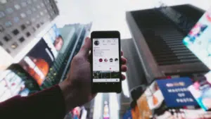 A person holding up a cell phone in front of a billboard.