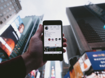 A person holding up a cell phone in front of a billboard.