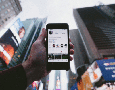 A person holding up a cell phone in front of a billboard.