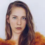 A young woman in an orange fur coat posing for a photo.