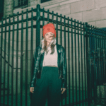 A woman wearing a red beanie standing in front of a fence.