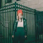 A woman wearing a red beanie standing in front of a fence.