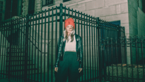 A woman wearing a red beanie standing in front of a fence.
