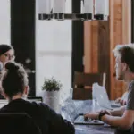 A group of people sitting around a table with laptops.