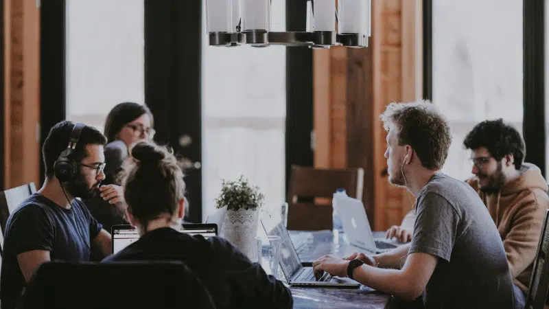 A group of people sitting around a table with laptops.