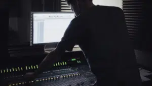 A man working on a mixing console in a recording studio.