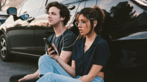 A young couple sitting next to a car listening to music.