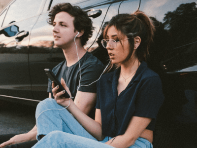 A young couple sitting next to a car listening to music.