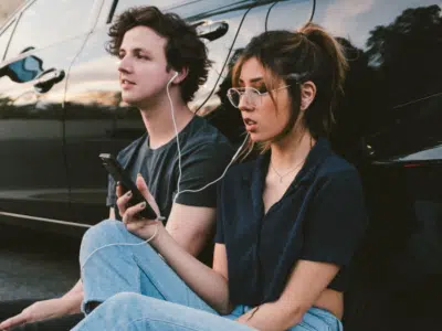 A young couple sitting next to a car listening to music.