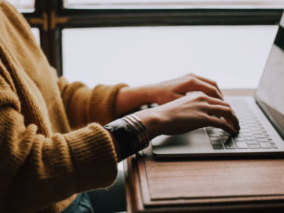 A woman typing on a laptop in front of a window.