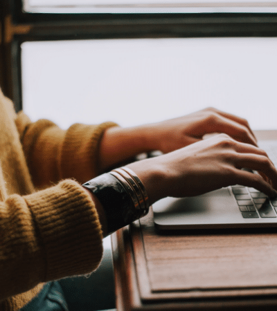 A woman typing on a laptop in front of a window.