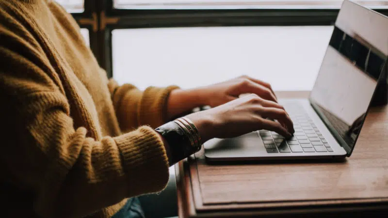 A woman typing on a laptop in front of a window.