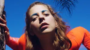 A woman in an orange shirt leaning against a tree.