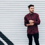 A man in a burgundy shirt leaning against a wall.