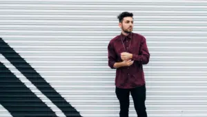 A man in a burgundy shirt leaning against a wall.