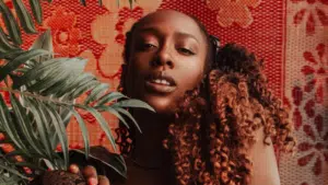 A woman with curly hair posing in front of a red pattern.