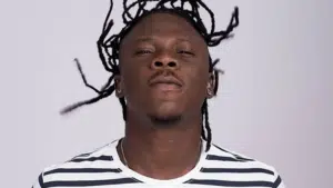 A man with dreadlocks is standing in front of a white background.