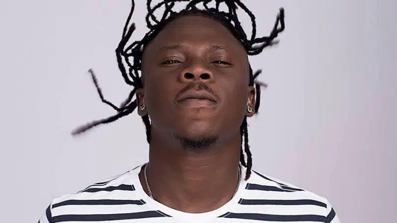 A man with dreadlocks is standing in front of a white background.