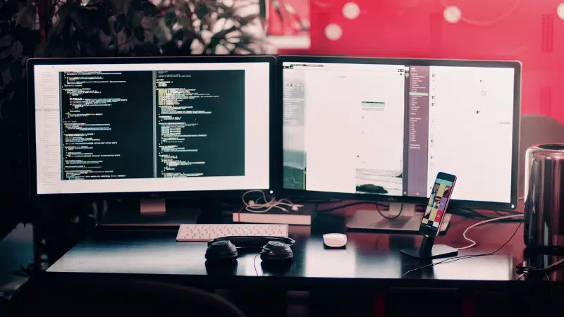 A desk with two monitors and a mouse.