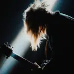 A person with long hair playing a guitar in a dark room.