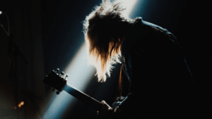 A person with long hair playing a guitar in a dark room.