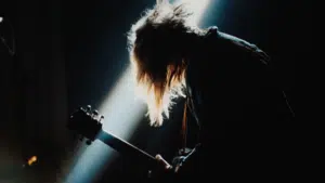 A person with long hair playing a guitar in a dark room.