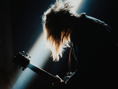 A person with long hair playing a guitar in a dark room.