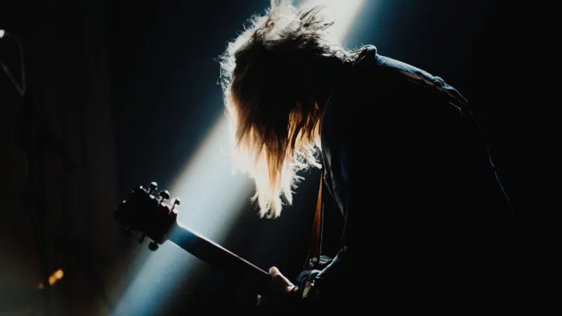 A person with long hair playing a guitar in a dark room.