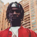 A man with dreadlocks standing in front of buildings.