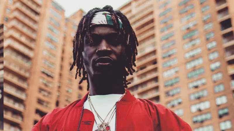 A man with dreadlocks standing in front of buildings.