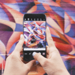 A person taking a photo of graffiti on a cell phone.