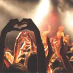 A crowd at a concert making a heart shape with their hands.