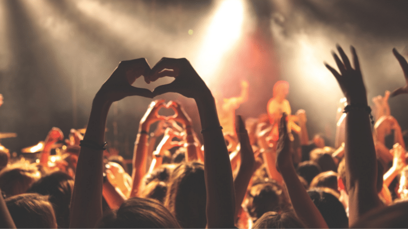 A crowd at a concert making a heart shape with their hands.