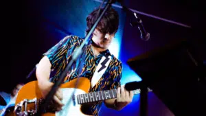 A man is playing an electric guitar in front of a microphone.