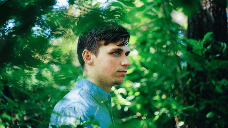 A man in a blue shirt is standing in the woods.