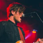 A man playing an electric guitar in front of a microphone.