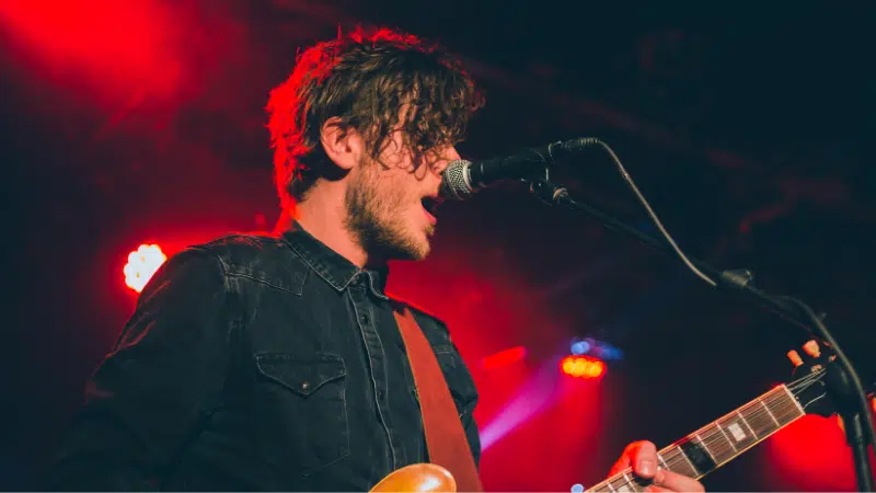 A man playing an electric guitar in front of a microphone.