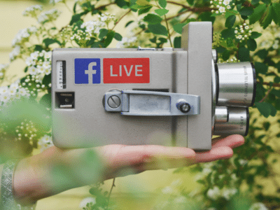 A person holding a camera with the facebook live logo on it.