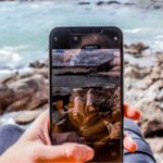 A person holding up a phone with a picture of the ocean.