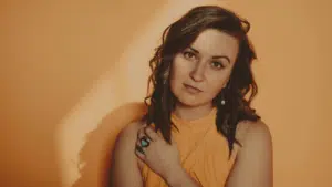 A woman is posing in front of an orange wall.